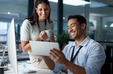 A picture of a man showing something on his tablet to a woman, and both of them sharing a laugh.