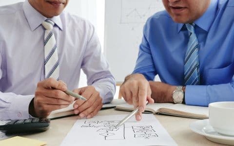 A picture of two persons discussing something about a chart drawn on paper.